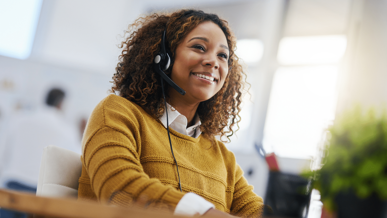 Smiling customer service representative wearing a headset, sitting at a desk and assisting customers in a bright modern office